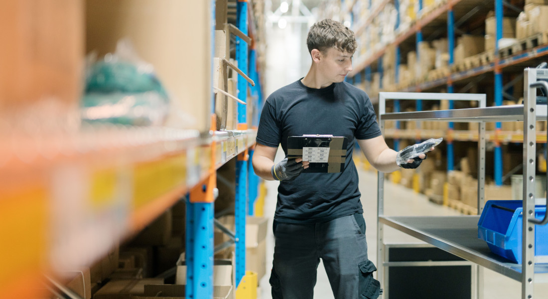 Mitarbeiter bei der Kommissionierung im Lager von EFB-Elektronik mit Produkt und Klemmbrett zwischen Hochregalen