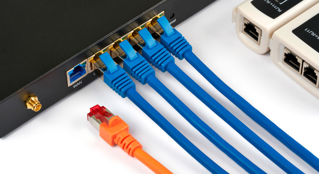 Netzwerk-Switch mit angeschlossenen blauen Netzwerkkabeln und einem orangefarbenen Netzwerkkabel. Netzwerk-Switch mit angeschlossenen blauen Netzwerkkabeln und einem orangefarbenen Netzwerkkabel.