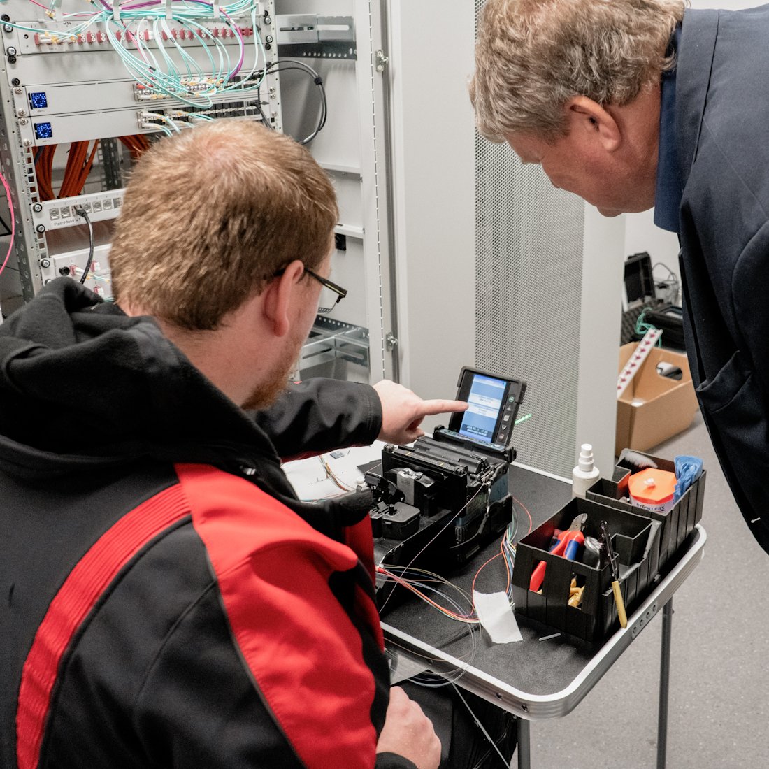 Techniker erklärt Glasfaser-Verteiler im Serverschrank – professionelle Netzwerkinstallation mit strukturierter Glasfaserverkabelung