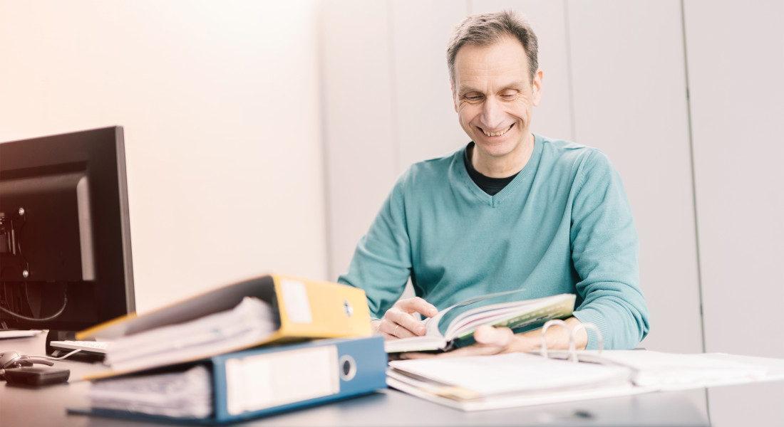 EFB-Elektronik employee in the office at a table. Folders are lying on the table. The employee looks something up and rummages through the documents.