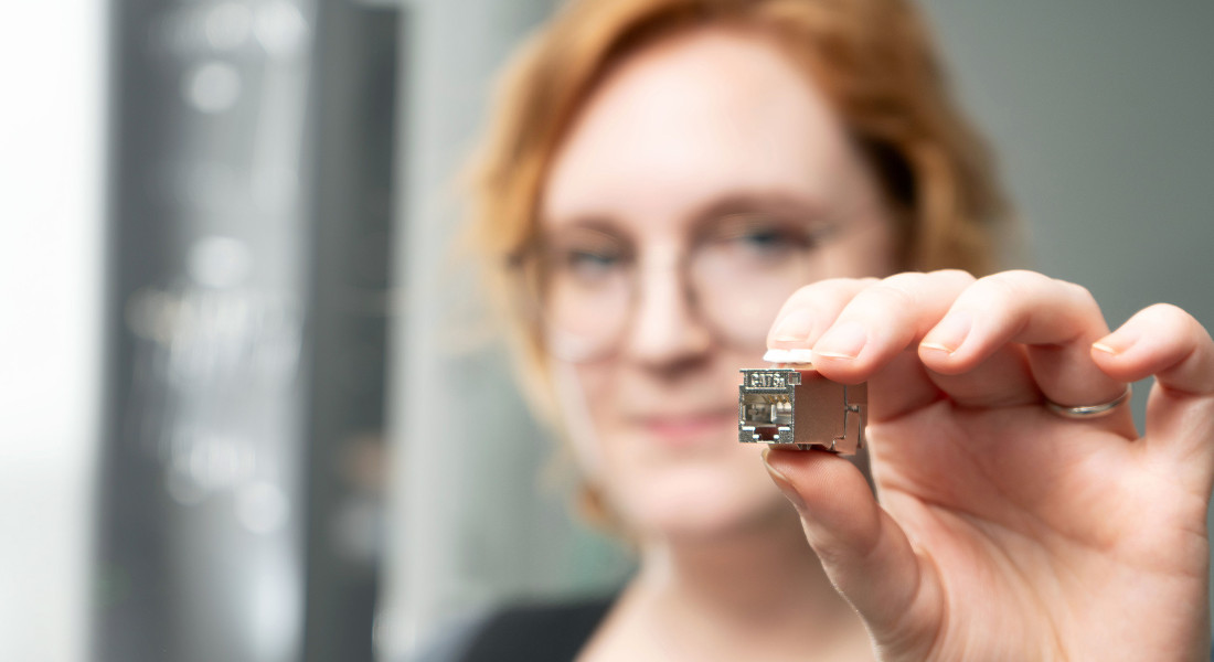 Red-haired woman with round glasses holds RJ45 Keystone Slimline/ Shortbody Cat.6A in her hand