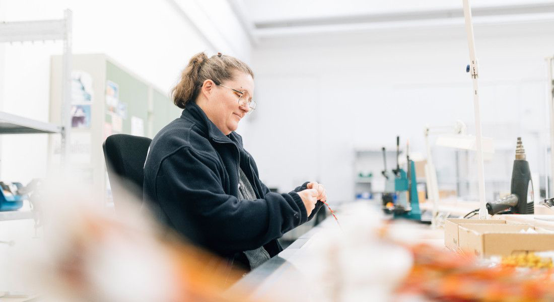 Frau bearbeitet Kabel an einem Arbeitsplatz in einer Produktionshalle.