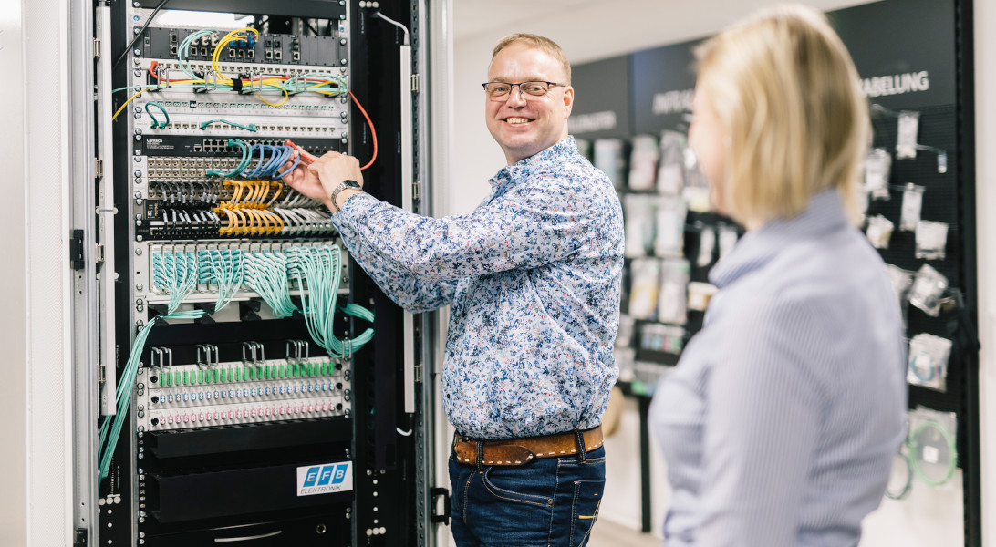 EFB-Elektronik's product manager stands at a server cabinet in a relaxed and friendly manner. He is in conversation with a colleague.