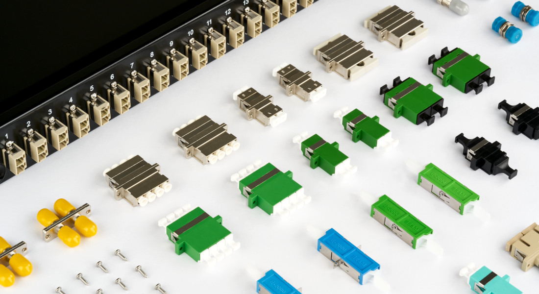 Verschiedene Glasfaser-Kupplungen vor einem Patchpanel mit nummerierten Ports. Verschiedene Glasfaser-Kupplungen vor einem Patchpanel mit nummerierten Ports.