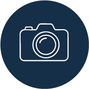White line drawing of a camera with a lens on a dark blue, round background.