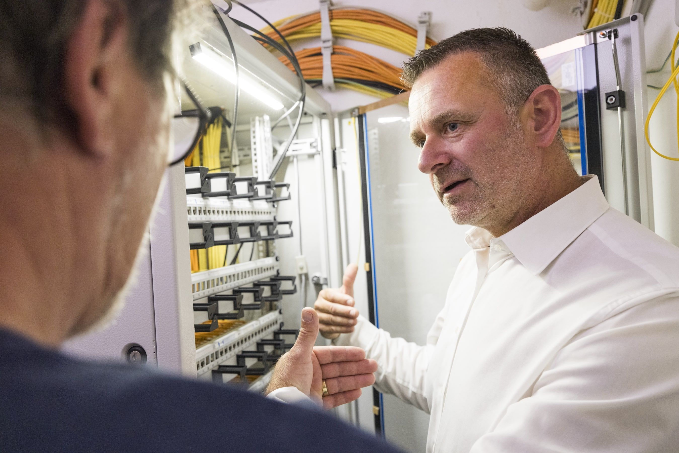 Fachgespräch vor Netzwerkschrank mit strukturierter Verkabelung und Glasfaserkabeln