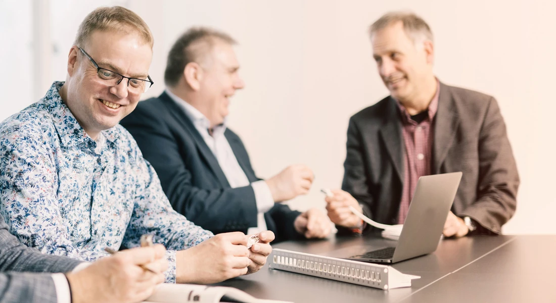 Drei Fachberater besprechen ein Patchpanel und Netzwerktechnik am Besprechungstisch.