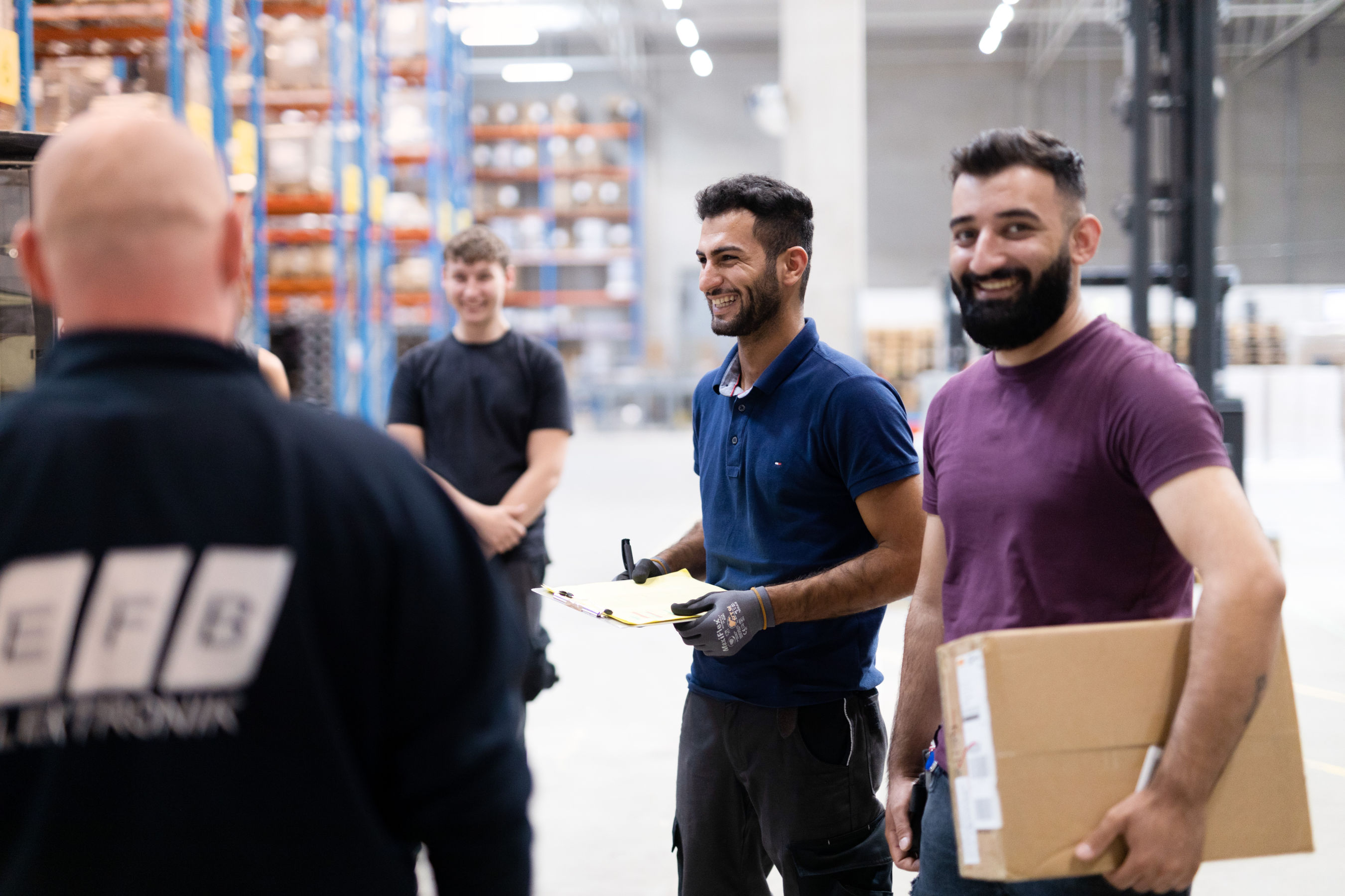 Teammeeting im Lager von EFB-Elektronik mit Mitarbeitenden im Austausch und Paketübergabe in freundlicher Atmosphäre