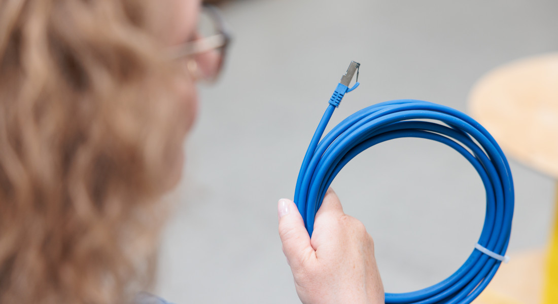 Frau hält blaues Netzwerkkabel mit RJ45-Stecker. Frau hält blaues Netzwerkkabel mit RJ45-Stecker.