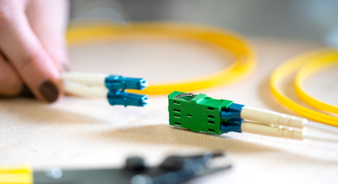 Hand holding fiber optic cable and green fiber optic coupling, yellow fiber optic cable in the background. Hand holding fiber optic cable and green fiber optic coupling, yellow fiber optic cable in the background.