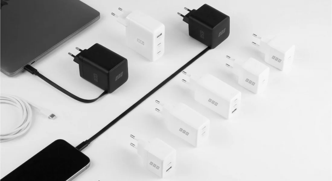 Mehrere USB-C Ladegeräte in Schwarz und Weiß mit 65W und 100W auf weißem Hintergrund, daneben Smartphone, Tablet und USB-C Ladekabel