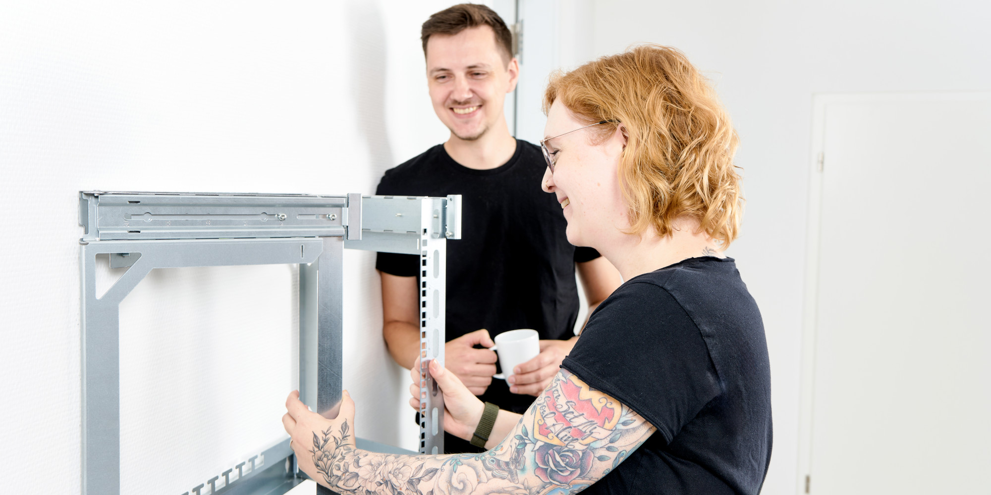 Frau klappt X-Rack aus, während ihr Kollege Kaffee trinkt Frau klappt X-Rack aus, während ihr Kollege Kaffee trinkt