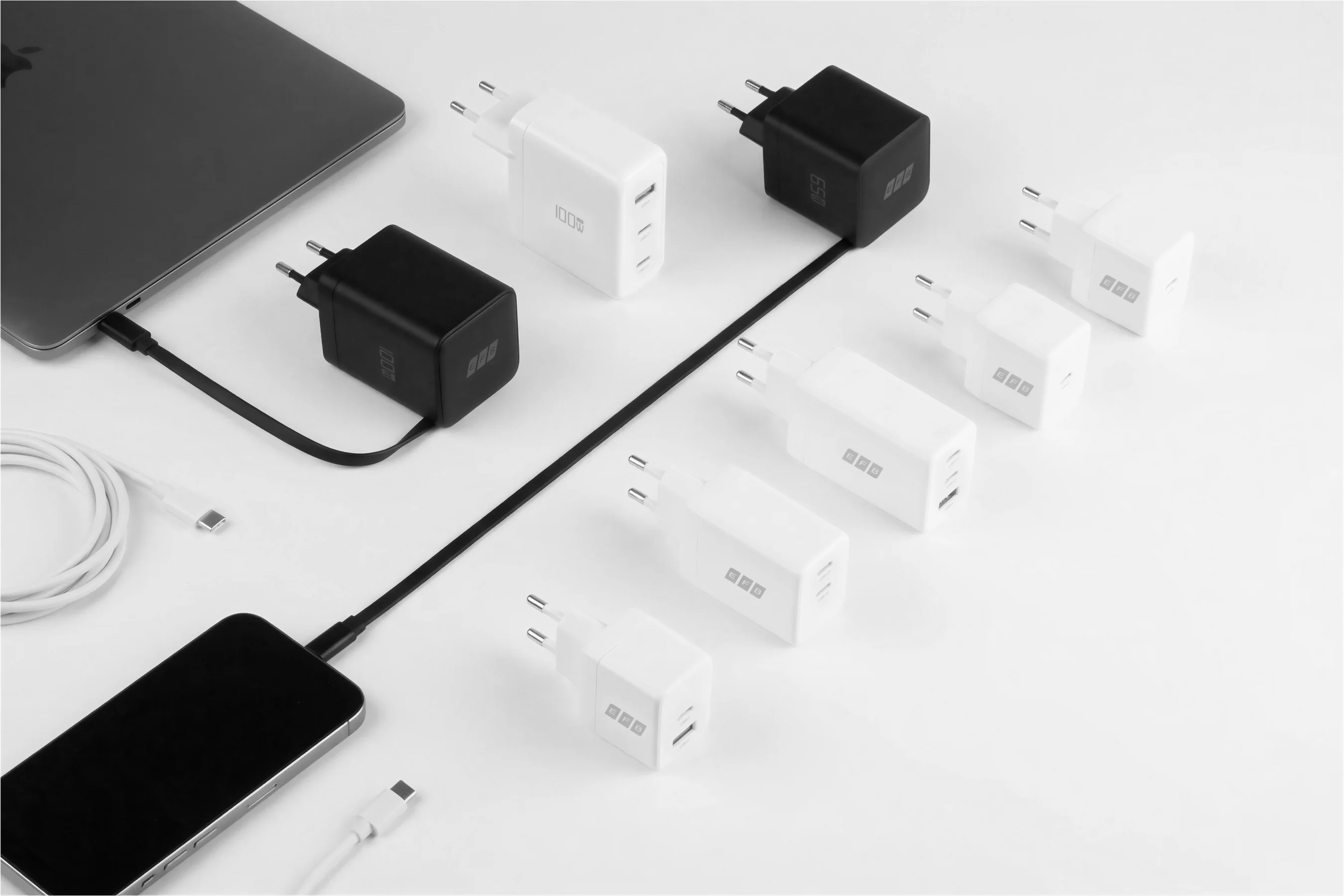 Mehrere USB-C Ladegeräte in Schwarz und Weiß mit 65W und 100W auf weißem Hintergrund, daneben Smartphone, Tablet und USB-C Ladekabel